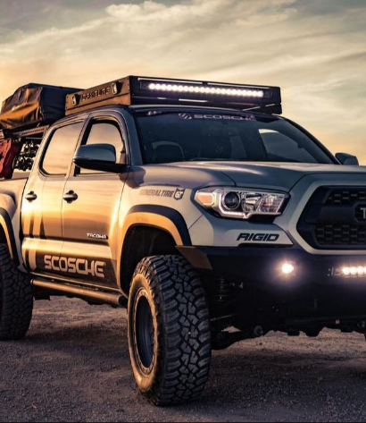 A rugged truck equipped with light bar and luggage rack sitting off road.
