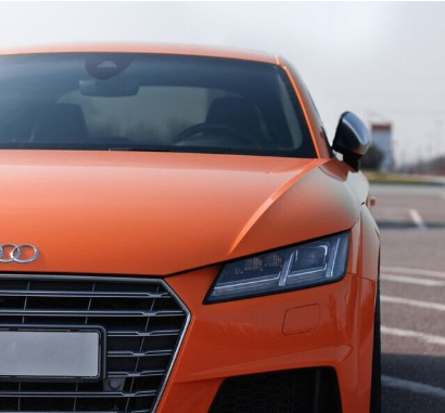 A bright orange Audi with tinted glass park in a lot.
