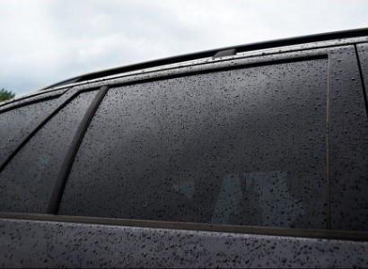 A close up photo of a dark shade of window tint with light droplets of rain on it.